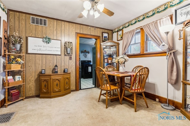 carpeted dining room with ceiling fan, baseboards, visible vents, and wooden walls