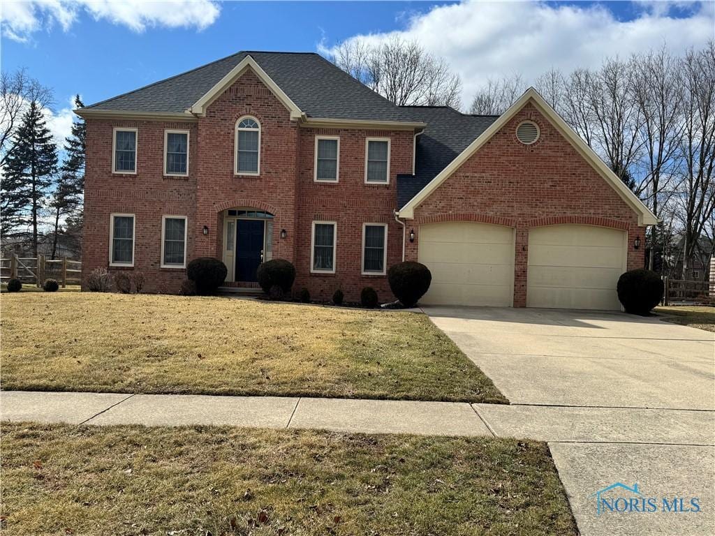 colonial house with a garage, concrete driveway, brick siding, and a front lawn