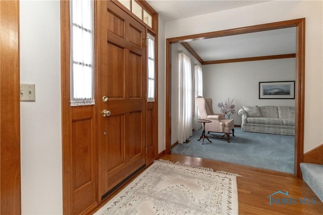 foyer entrance with crown molding, baseboards, and wood finished floors