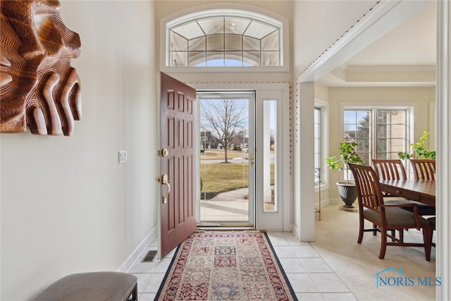 foyer entrance with baseboards, plenty of natural light, light tile patterned flooring, and crown molding