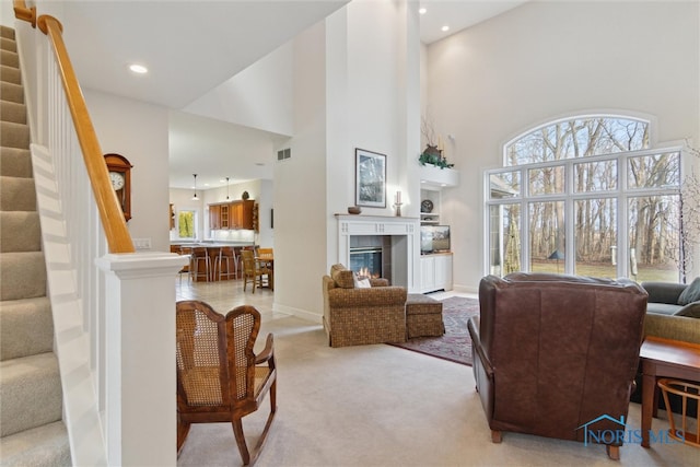 carpeted living area featuring a wealth of natural light, stairs, visible vents, and a tiled fireplace