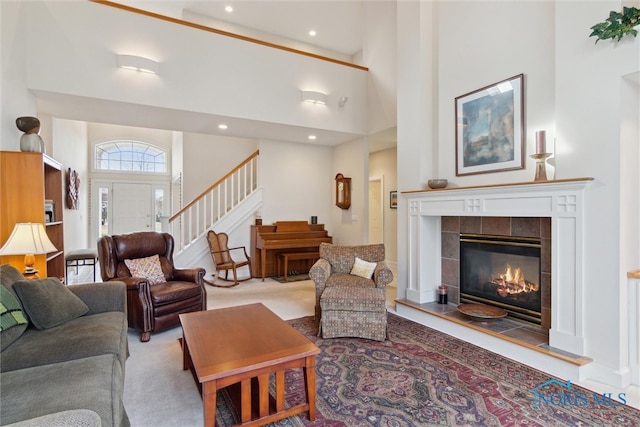 carpeted living area with a tile fireplace, recessed lighting, a high ceiling, and stairs