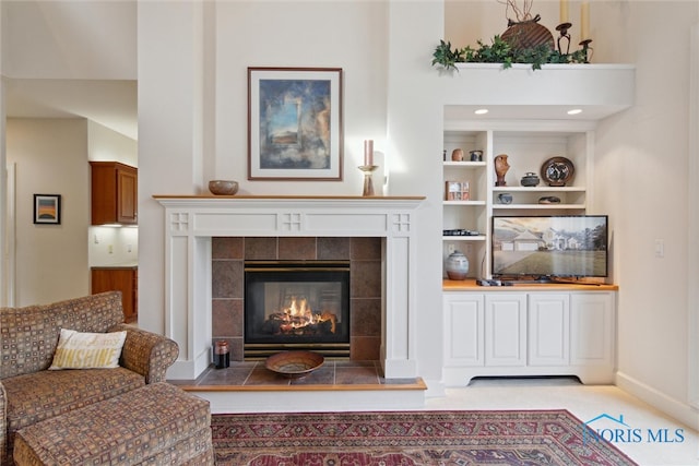 living area featuring built in shelves, a tile fireplace, and baseboards