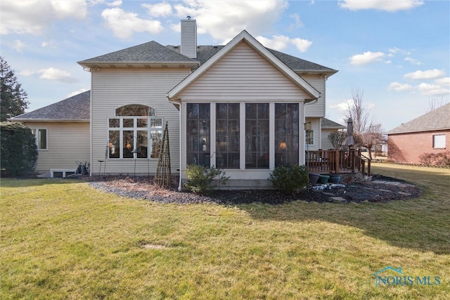 back of property with a sunroom, roof with shingles, a lawn, and a chimney