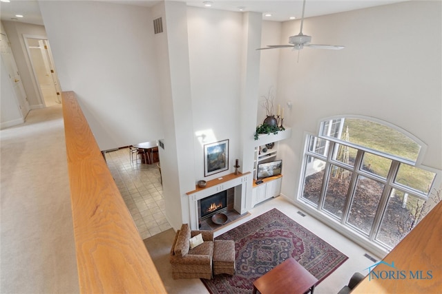 living area featuring visible vents, a ceiling fan, light colored carpet, a towering ceiling, and a fireplace