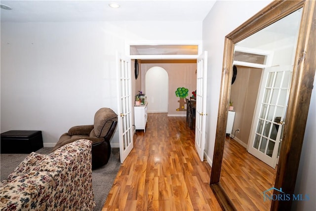 hallway featuring arched walkways, french doors, baseboards, and light wood-style floors