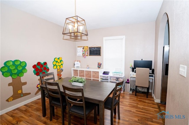 dining room with arched walkways, an inviting chandelier, baseboards, and wood finished floors