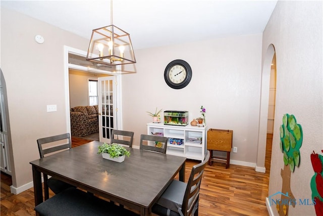 dining area featuring arched walkways, a notable chandelier, wood finished floors, and baseboards