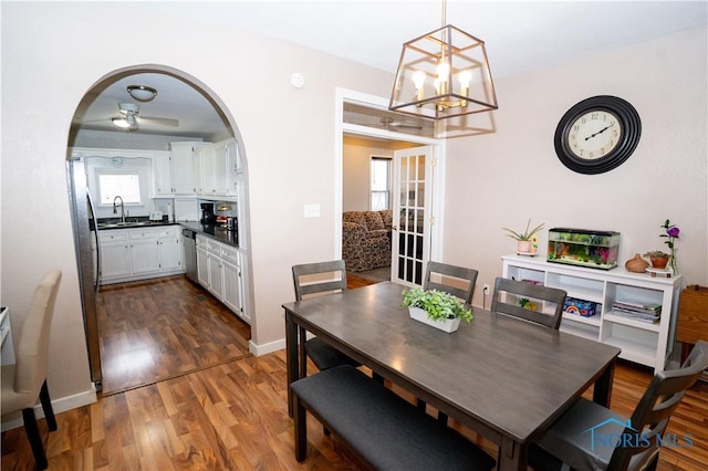 dining space with an inviting chandelier, baseboards, arched walkways, and wood finished floors