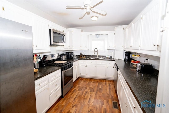 kitchen featuring stainless steel appliances, a ceiling fan, white cabinets, a sink, and wood finished floors