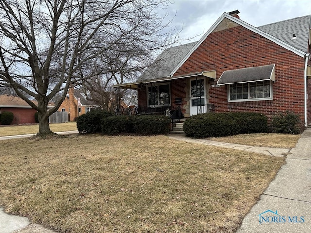 bungalow featuring a shingled roof, covered porch, brick siding, and a front lawn