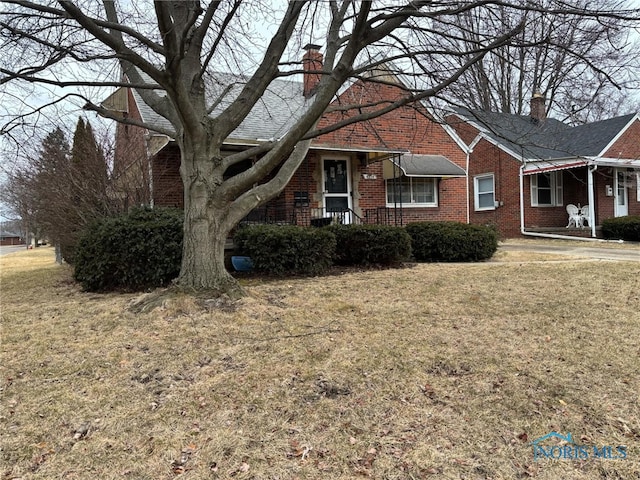 view of front of house with a front yard, brick siding, and a chimney