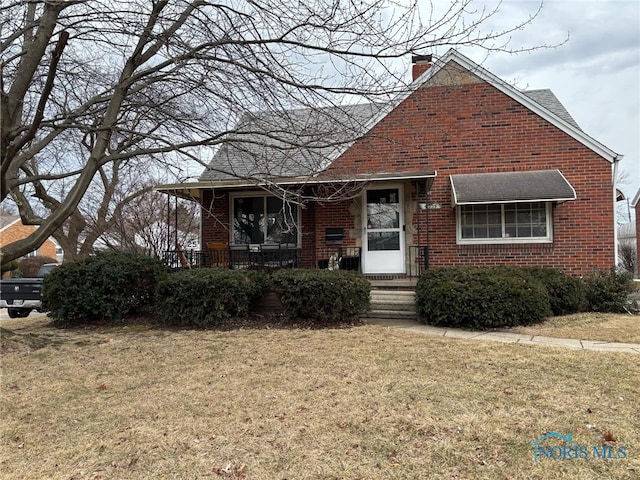 view of front facade with a chimney, roof with shingles, a front lawn, a porch, and brick siding