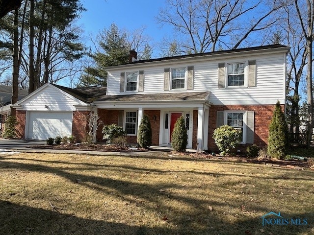 traditional-style home featuring brick siding, a chimney, a garage, driveway, and a front lawn