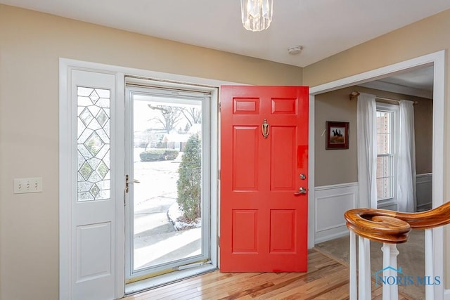 entryway with a healthy amount of sunlight, light wood-style floors, a decorative wall, and a wainscoted wall