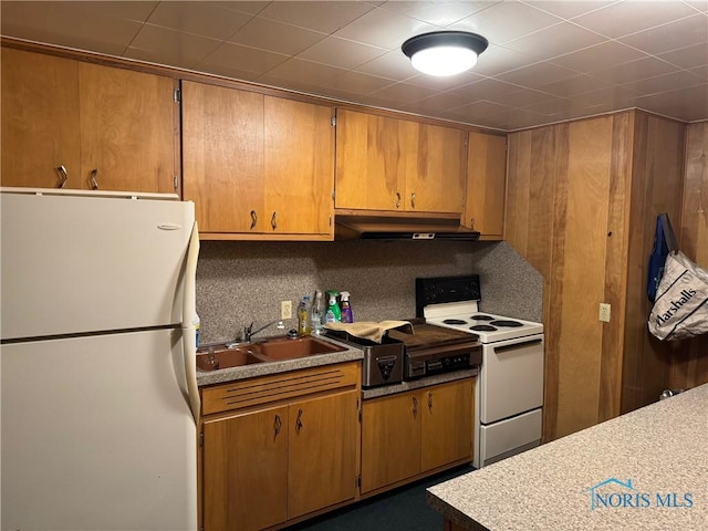 kitchen with white appliances, brown cabinetry, backsplash, under cabinet range hood, and a sink