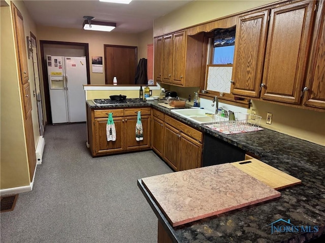 kitchen featuring white refrigerator with ice dispenser, brown cabinets, a peninsula, a baseboard heating unit, and a sink