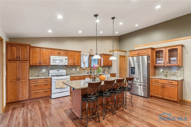 kitchen featuring white appliances, a kitchen island, glass insert cabinets, brown cabinets, and a kitchen breakfast bar