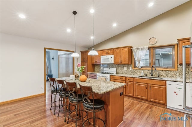 kitchen featuring white appliances, brown cabinetry, light stone counters, a breakfast bar, and a sink