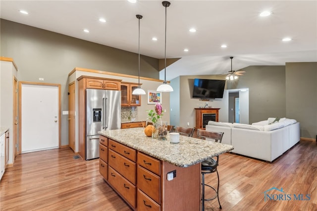 kitchen with a fireplace, high end fridge, light wood-style floors, a kitchen island, and a kitchen breakfast bar