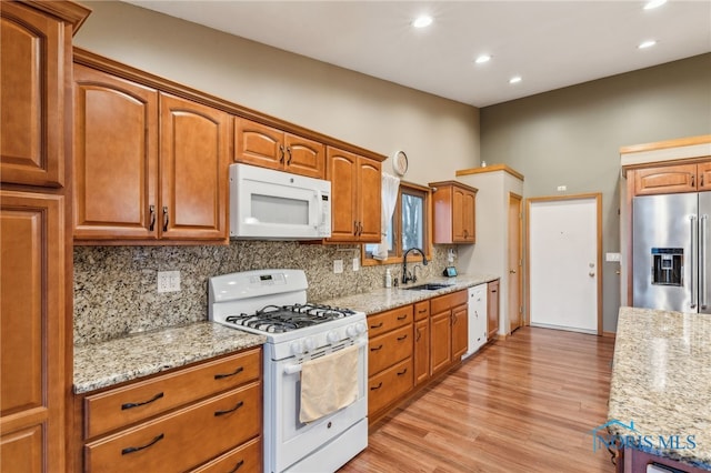 kitchen featuring white appliances, light stone counters, backsplash, and a sink