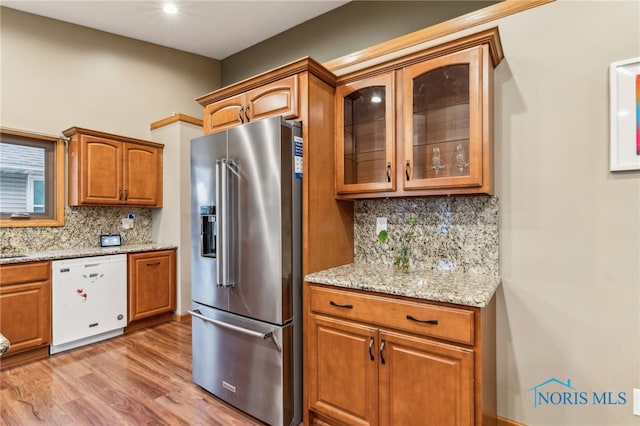 kitchen with light stone counters, high end refrigerator, dishwasher, brown cabinetry, and glass insert cabinets