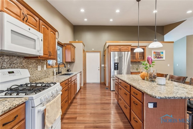 kitchen featuring a center island, a sink, light stone countertops, light wood-type flooring, and white appliances