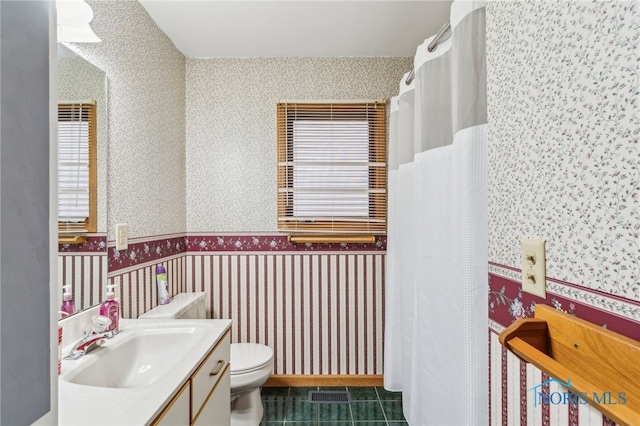 full bath with a wainscoted wall, visible vents, toilet, vanity, and wallpapered walls