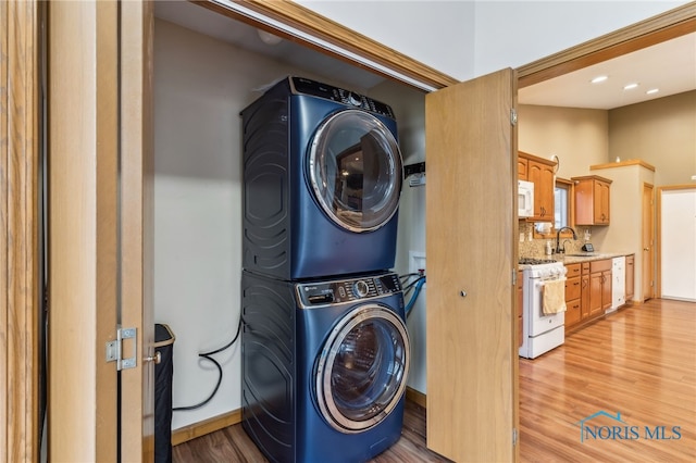 laundry area with laundry area, a sink, light wood-style flooring, and stacked washer / drying machine