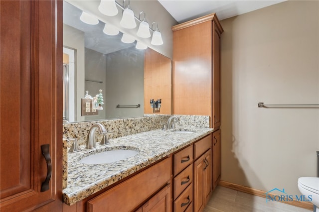 bathroom with double vanity, a sink, toilet, and baseboards