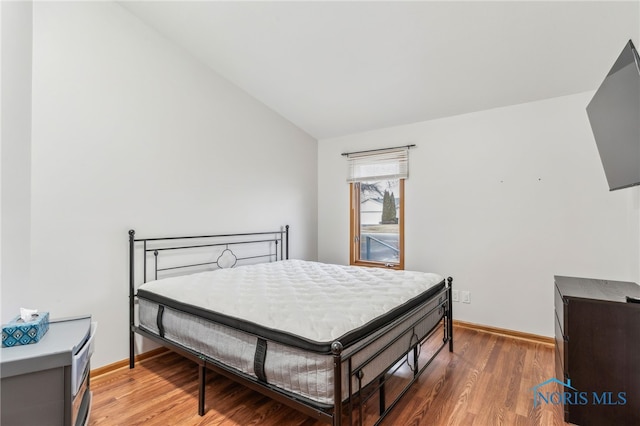 bedroom featuring light wood-type flooring, lofted ceiling, and baseboards