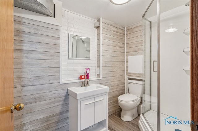 bathroom with toilet, wood finished floors, vanity, wood walls, and a shower stall