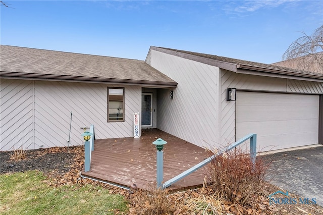 exterior space with aphalt driveway, a shingled roof, a deck, and an attached garage