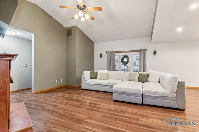 living room featuring light wood finished floors, baseboards, visible vents, a ceiling fan, and vaulted ceiling