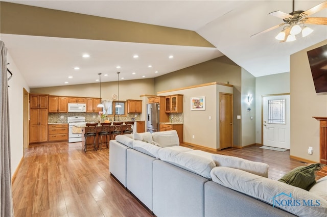 living area featuring lofted ceiling, baseboards, and light wood finished floors