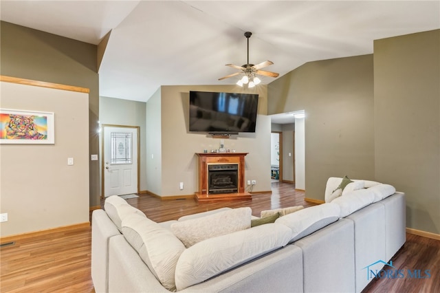 living area with a fireplace with raised hearth, ceiling fan, wood finished floors, baseboards, and vaulted ceiling