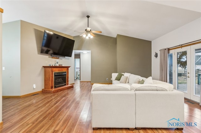 living room with a fireplace with raised hearth, ceiling fan, light wood-style flooring, vaulted ceiling, and french doors