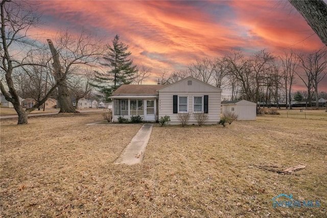 view of front of property with a yard, a sunroom, an outdoor structure, and a storage shed