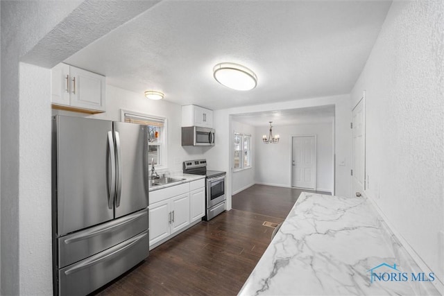 kitchen featuring dark wood finished floors, stainless steel appliances, a textured ceiling, white cabinetry, and a notable chandelier