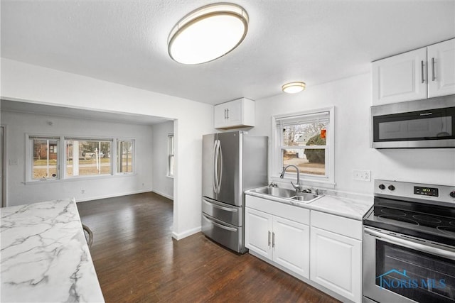 kitchen with white cabinets, dark wood-type flooring, stainless steel appliances, and a sink