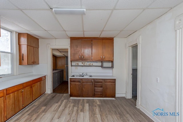 kitchen featuring light countertops, brown cabinetry, a drop ceiling, and wood finished floors