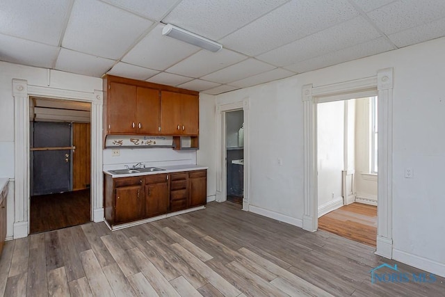 kitchen with brown cabinets, a sink, a drop ceiling, and wood finished floors