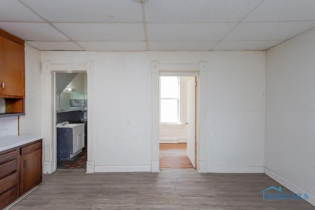 interior space featuring a paneled ceiling, baseboards, and wood finished floors