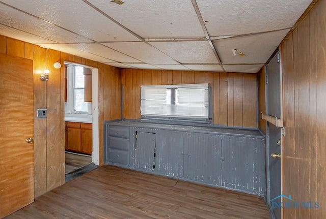 kitchen with wood walls, a drop ceiling, wood finished floors, and brown cabinets