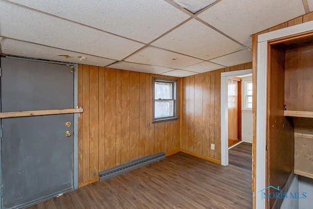 empty room with a paneled ceiling, wood walls, a baseboard radiator, and wood finished floors