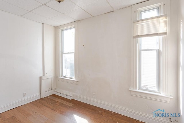 empty room featuring a paneled ceiling, visible vents, baseboards, and wood finished floors