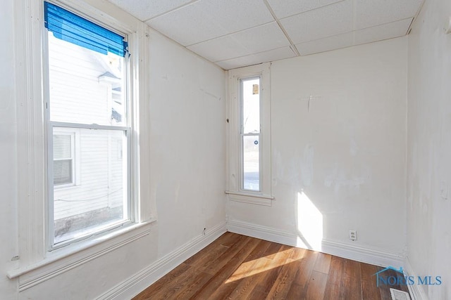 empty room with dark wood-style floors, a drop ceiling, and baseboards