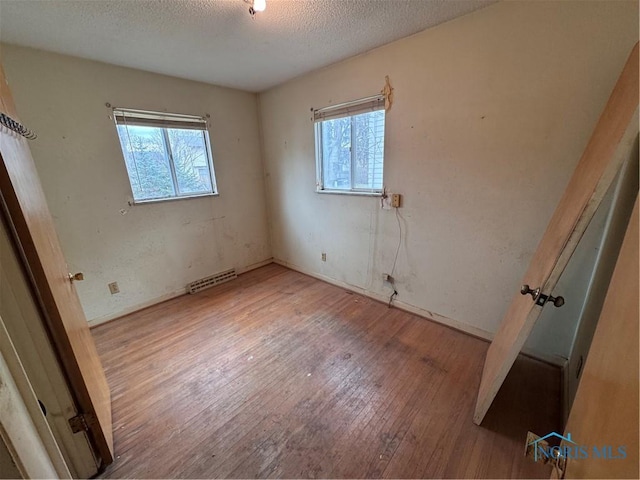 unfurnished bedroom with a textured ceiling, multiple windows, visible vents, and hardwood / wood-style floors