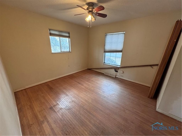 spare room featuring a textured ceiling, wood finished floors, a ceiling fan, and baseboards