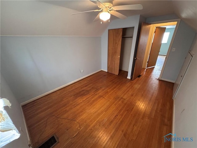 unfurnished bedroom with lofted ceiling, a closet, wood-type flooring, visible vents, and baseboards